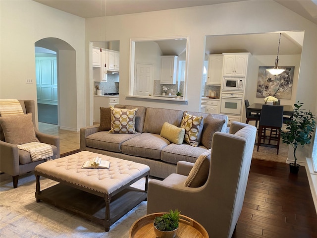 living area with arched walkways, vaulted ceiling, and dark wood-type flooring