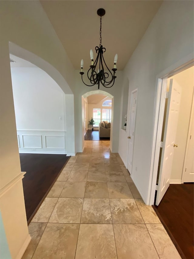 corridor featuring an inviting chandelier, arched walkways, wainscoting, and a high ceiling