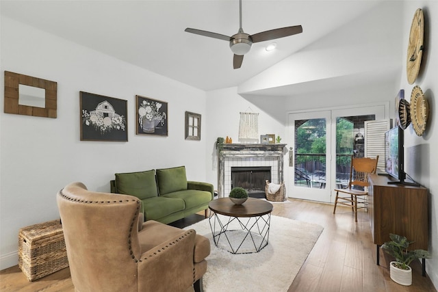 living area with ceiling fan, vaulted ceiling, a tiled fireplace, and wood finished floors