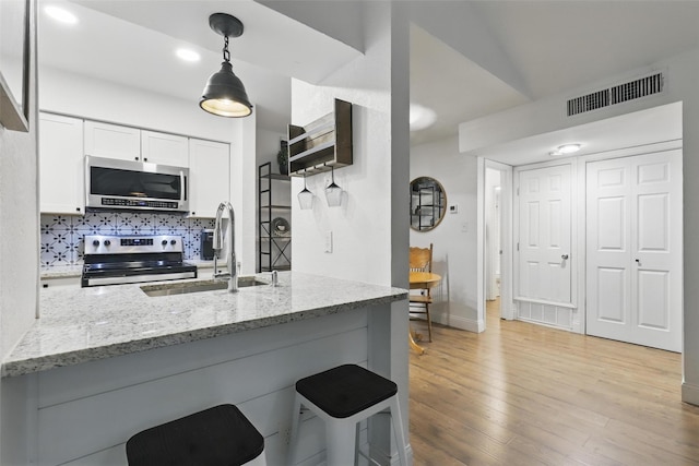 kitchen with visible vents, light stone counters, a sink, backsplash, and stainless steel appliances