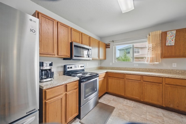 kitchen featuring brown cabinetry, light countertops, a textured ceiling, and stainless steel appliances