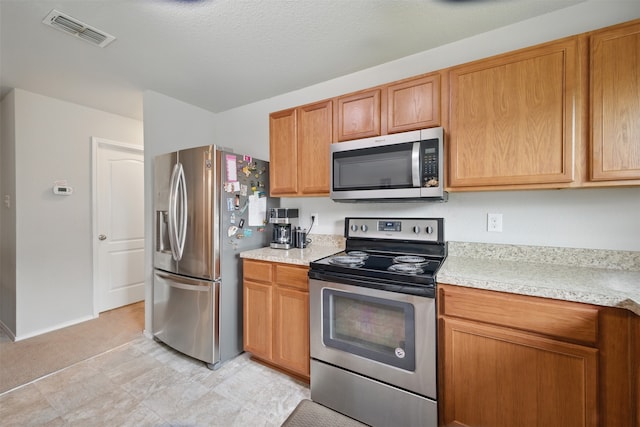 kitchen featuring visible vents, baseboards, light countertops, brown cabinets, and appliances with stainless steel finishes