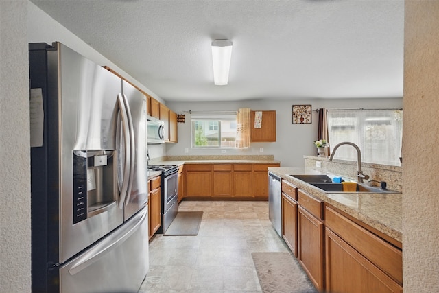 kitchen with light countertops, stainless steel appliances, brown cabinetry, and a sink