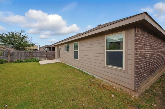 view of home's exterior featuring brick siding, a lawn, fence, and a patio