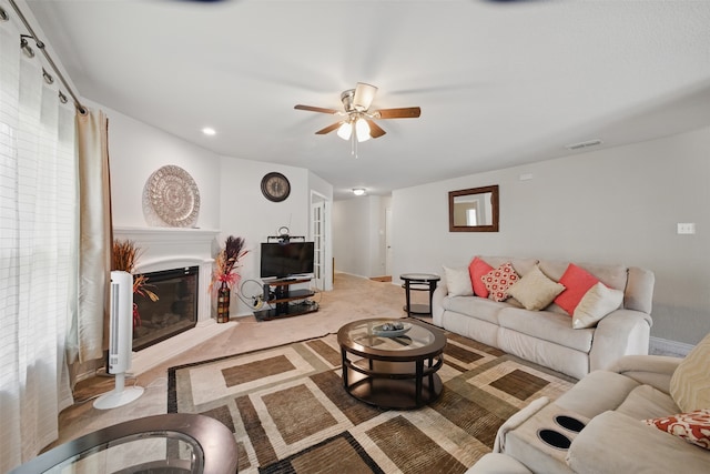 living area with ceiling fan, light colored carpet, a glass covered fireplace, baseboards, and visible vents