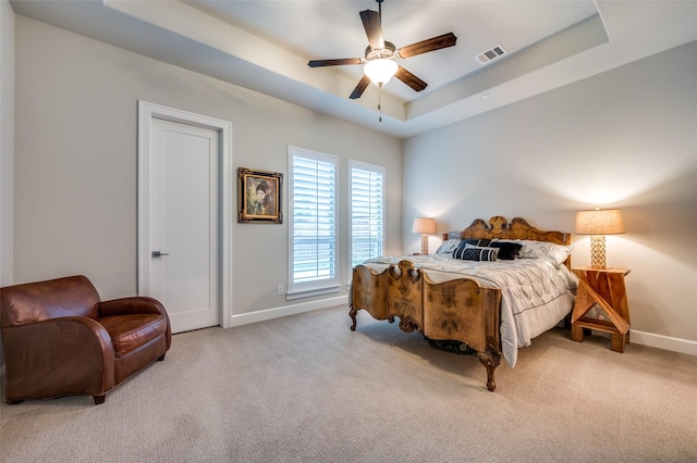 carpeted bedroom featuring ceiling fan, a tray ceiling, visible vents, and baseboards