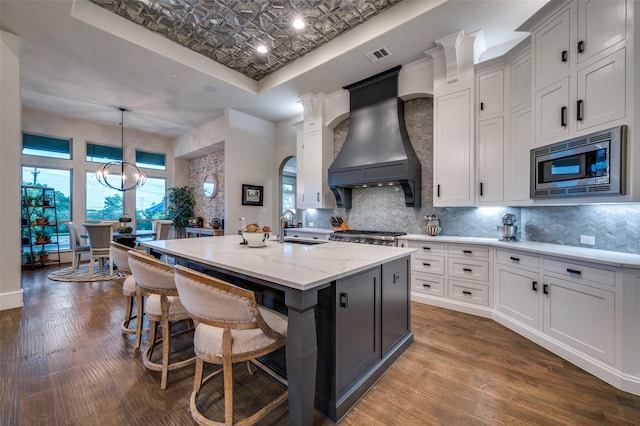 kitchen featuring a sink, premium range hood, stainless steel microwave, a tray ceiling, and visible vents
