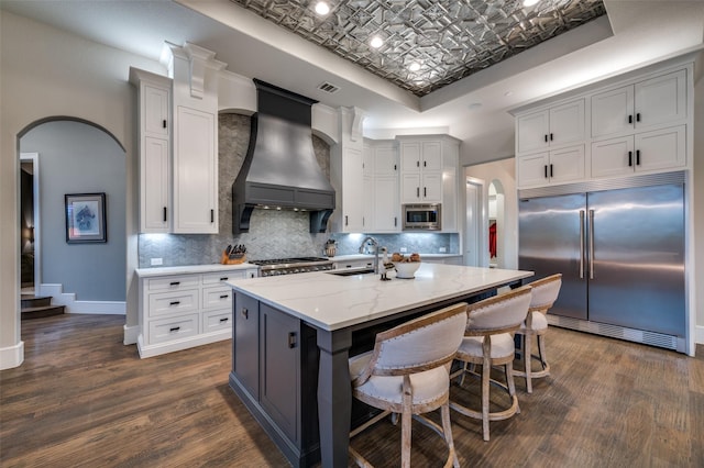 kitchen featuring a sink, built in appliances, an ornate ceiling, premium range hood, and a tray ceiling