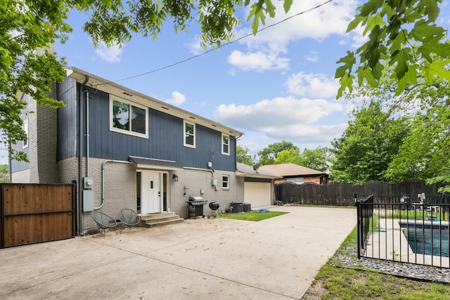 rear view of property featuring a garage, fence, brick siding, a gate, and driveway