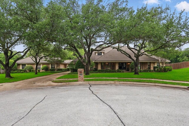 view of front facade with a tiled roof, fence, concrete driveway, and a front lawn