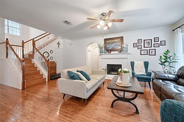 living room featuring a ceiling fan, light wood finished floors, arched walkways, and a fireplace
