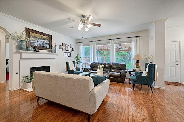 living area featuring light wood finished floors, arched walkways, a ceiling fan, a tile fireplace, and ornamental molding