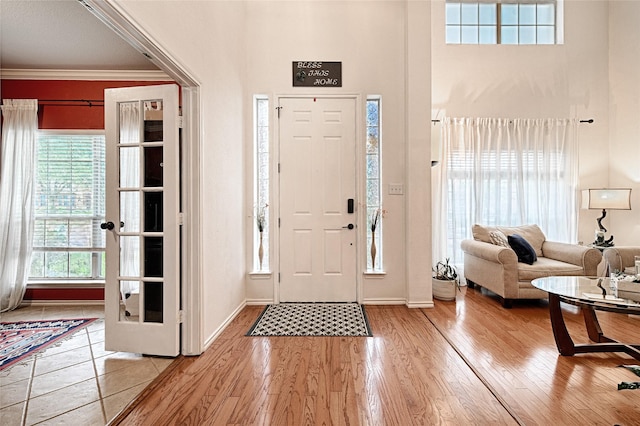 entryway featuring baseboards, light wood-style flooring, crown molding, and a high ceiling