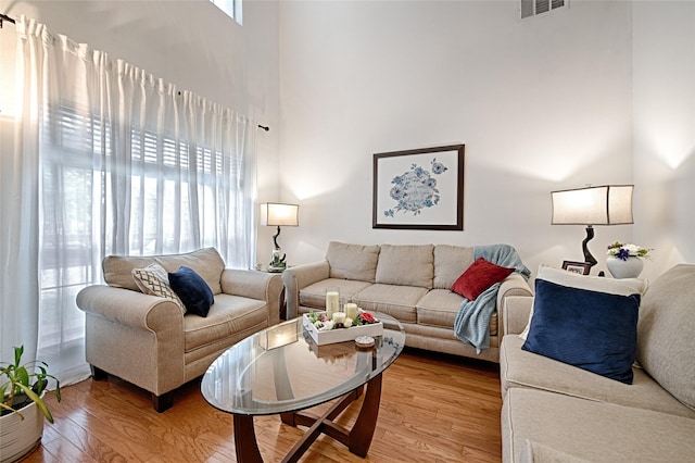 living room featuring visible vents, light wood-type flooring, and a towering ceiling