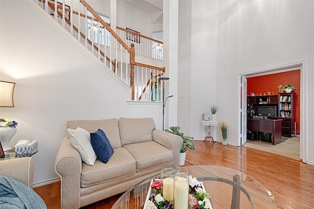 living area with baseboards, wood finished floors, stairway, and a towering ceiling