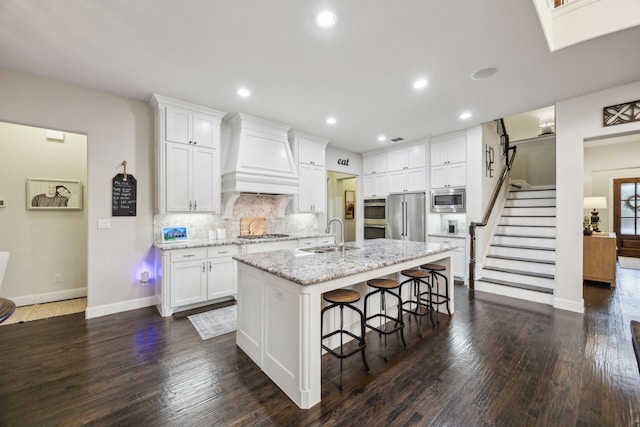 kitchen with custom exhaust hood, baseboards, a kitchen bar, a sink, and appliances with stainless steel finishes