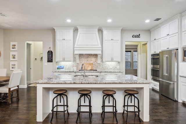 kitchen with appliances with stainless steel finishes, tasteful backsplash, a sink, white cabinets, and custom exhaust hood