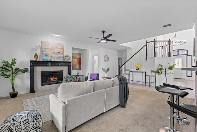 carpeted living area featuring visible vents, ornamental molding, a fireplace, stairway, and ceiling fan with notable chandelier