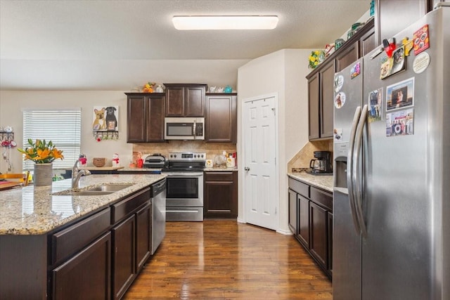 kitchen with dark wood-style flooring, dark brown cabinetry, appliances with stainless steel finishes, a sink, and tasteful backsplash