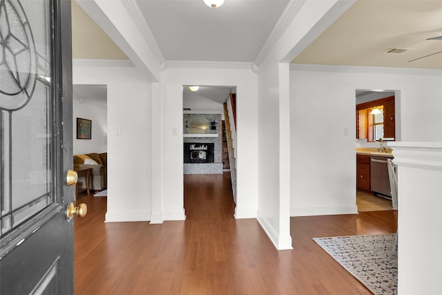 foyer featuring a large fireplace, baseboards, wood finished floors, visible vents, and ornamental molding
