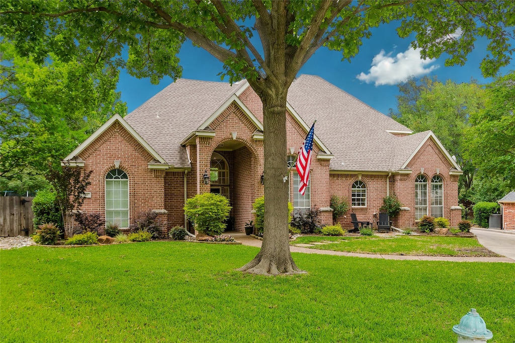 view of front of house featuring fence, a shingled roof, a front lawn, and brick siding