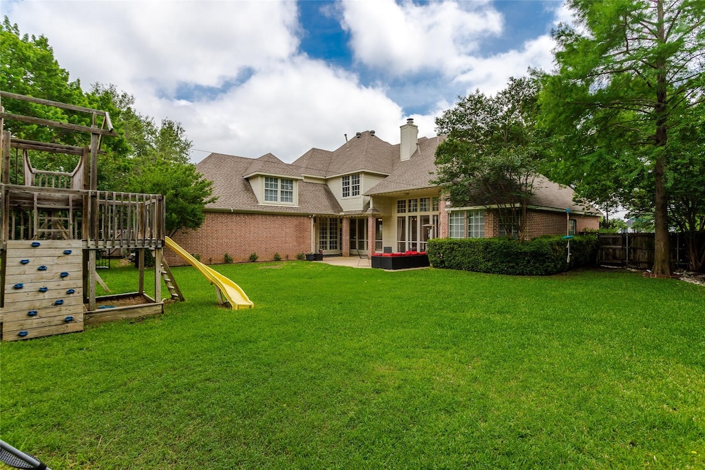 back of property featuring fence, brick siding, a chimney, a playground, and a yard