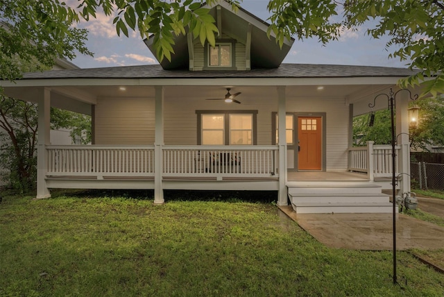 exterior space with covered porch, a ceiling fan, roof with shingles, fence, and a yard