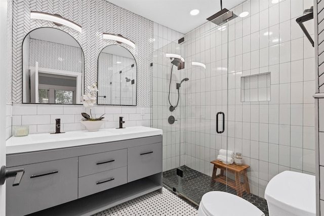 bathroom featuring double vanity, tile walls, a stall shower, a sink, and toilet