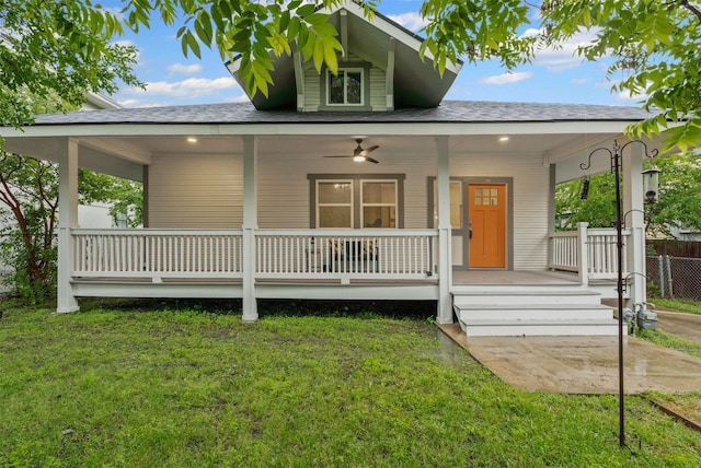 country-style home featuring a porch, fence, a shingled roof, and a front yard