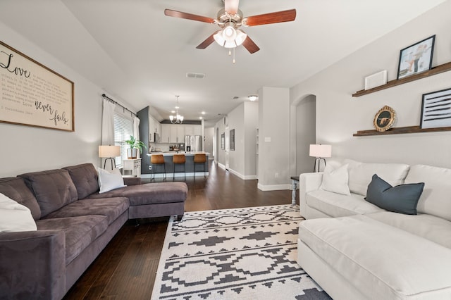 living area featuring visible vents, dark wood-style flooring, baseboards, arched walkways, and ceiling fan with notable chandelier