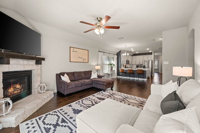 living room with visible vents, dark wood-style flooring, ceiling fan with notable chandelier, and a fireplace