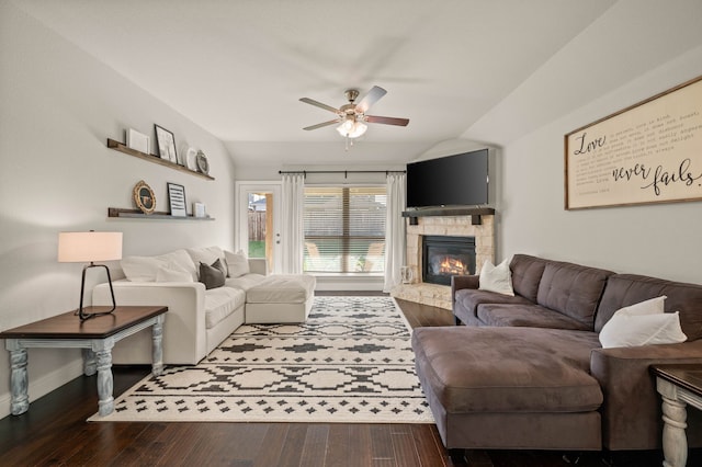 living room with ceiling fan, wood-type flooring, a stone fireplace, baseboards, and vaulted ceiling