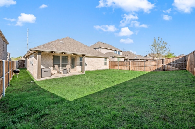 rear view of house with roof with shingles, a lawn, a patio area, brick siding, and a fenced backyard
