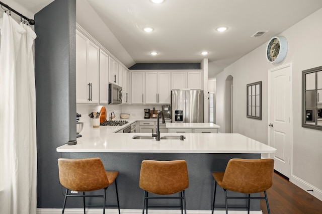kitchen with appliances with stainless steel finishes, a sink, arched walkways, dark wood finished floors, and a peninsula