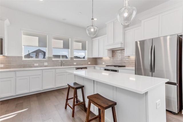 kitchen with a breakfast bar area, stainless steel appliances, white cabinetry, backsplash, and a kitchen island