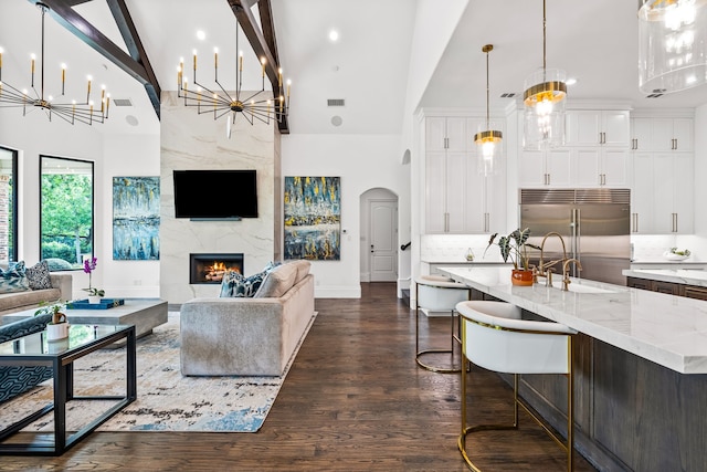 living room featuring dark wood-style floors, high vaulted ceiling, a high end fireplace, a chandelier, and arched walkways