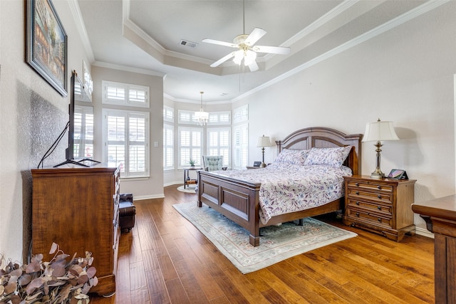 bedroom with visible vents, crown molding, a raised ceiling, baseboards, and wood-type flooring