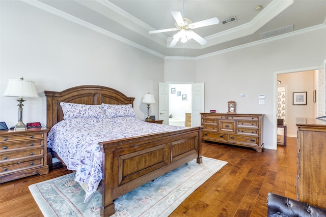 bedroom with wood-type flooring, crown molding, visible vents, and a raised ceiling