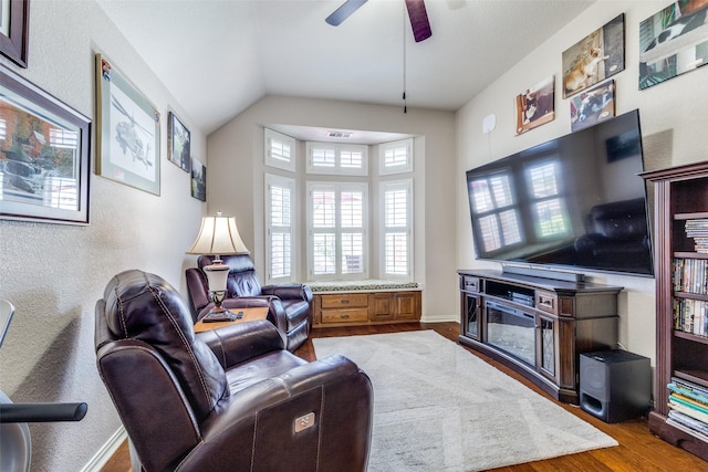 living room featuring a textured wall, a ceiling fan, wood finished floors, and lofted ceiling