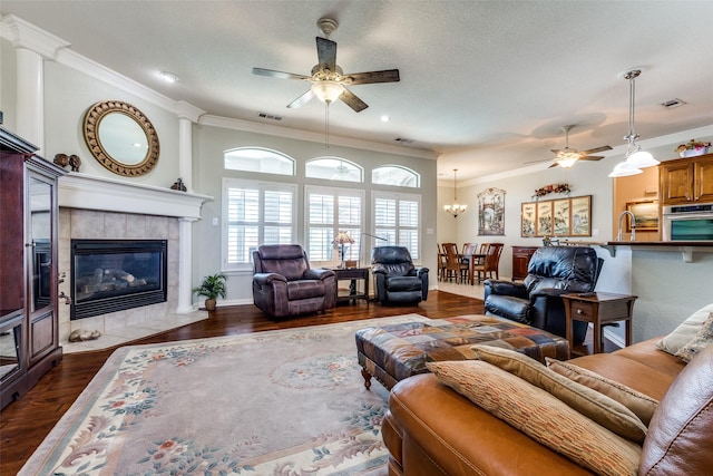 living room with crown molding, visible vents, ceiling fan with notable chandelier, and dark wood-type flooring