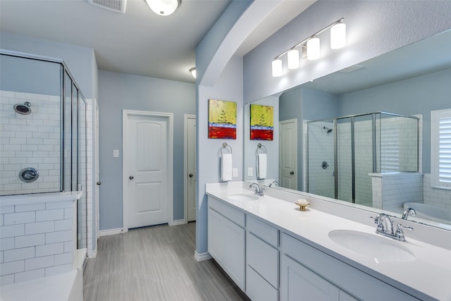 full bathroom featuring a sink, baseboards, a stall shower, and double vanity