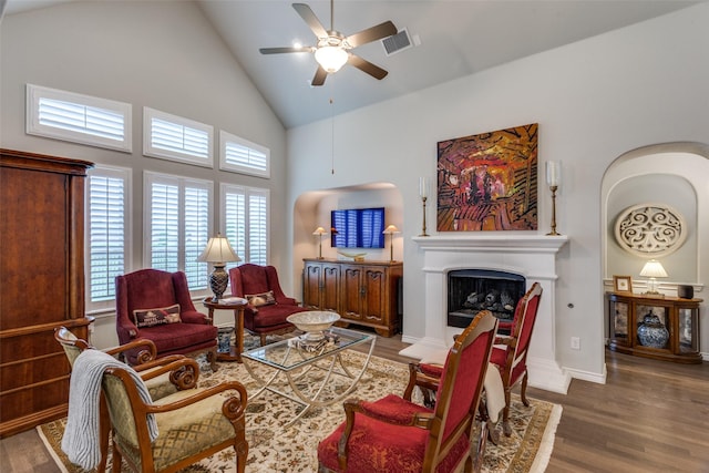 living room featuring ceiling fan, a fireplace with raised hearth, high vaulted ceiling, wood finished floors, and visible vents