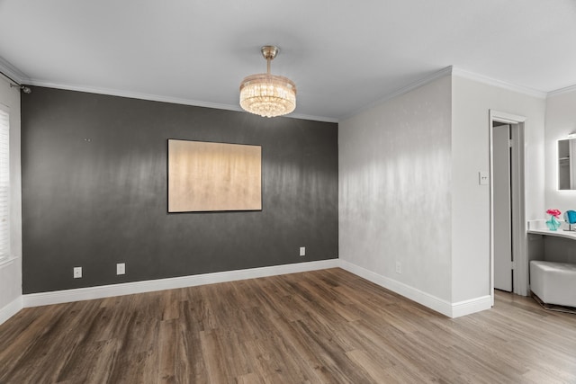 unfurnished room with an inviting chandelier, ornamental molding, baseboards, and wood finished floors