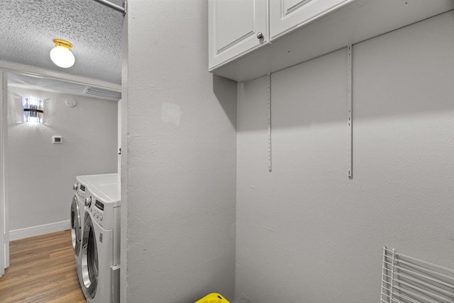 washroom featuring light wood-style floors, washer and clothes dryer, cabinet space, and baseboards