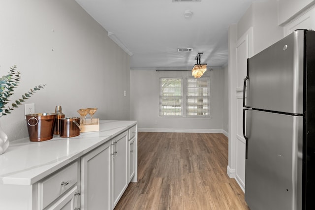 kitchen featuring visible vents, freestanding refrigerator, light wood-style floors, baseboards, and white cabinetry