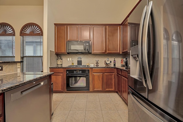 kitchen with tasteful backsplash, brown cabinets, light tile patterned floors, black appliances, and dark stone countertops
