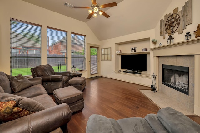 living room featuring ceiling fan, visible vents, wood finished floors, a tile fireplace, and vaulted ceiling