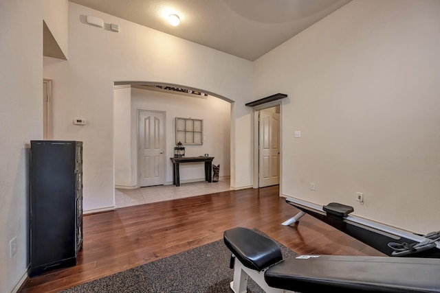 exercise room featuring arched walkways, baseboards, and wood finished floors
