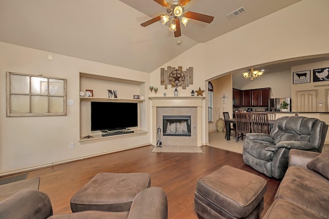 living room featuring visible vents, lofted ceiling, wood finished floors, a fireplace, and ceiling fan with notable chandelier