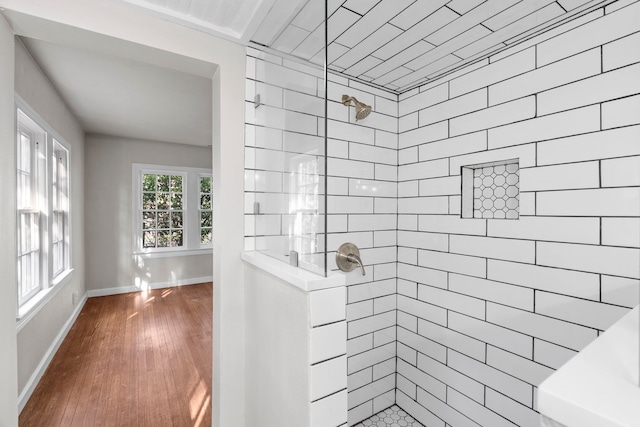 full bathroom featuring baseboards, a tile shower, and wood finished floors